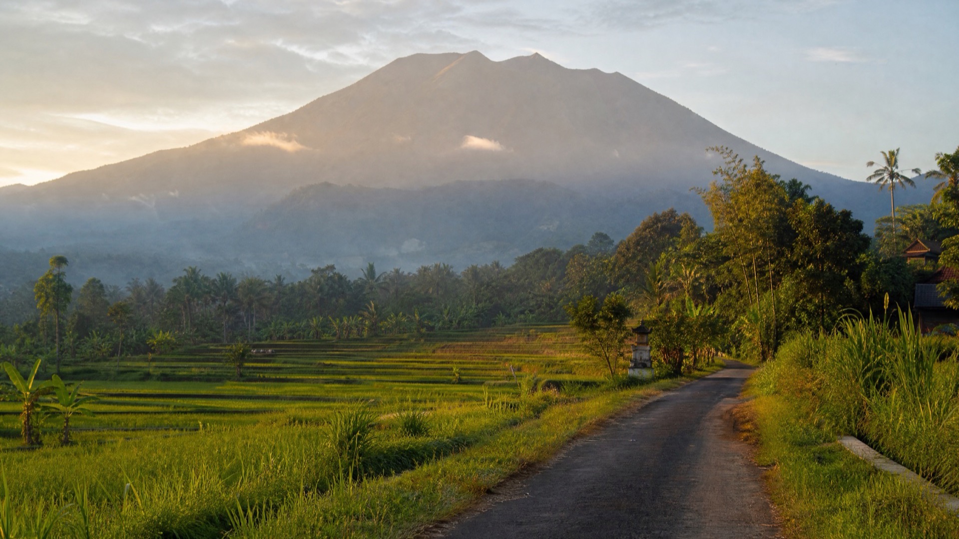 A quiet road through East Bali rice fields beneath Mount Agung in warm early-morning light